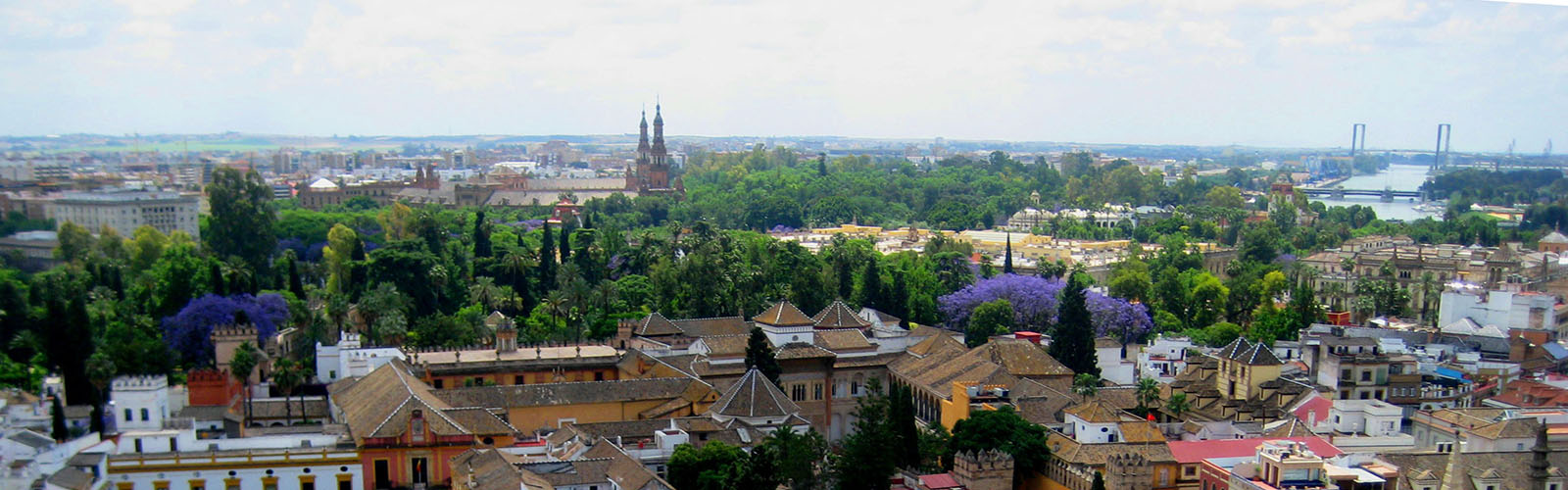 An aerial view of Seville, including densely-packed buildings, trees, and a large waterway in the distance.